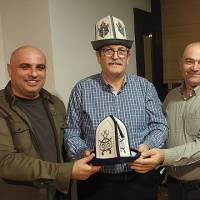 Serhat Duyar ile Çetin Mut birlikte Kırgızistan’dan getirilen Ak Kalpaklarını Ecz. Selçuk Arslan’a takdim ederken
